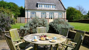 Een huis met een grote tuin en een ronde tafel met stoelen.