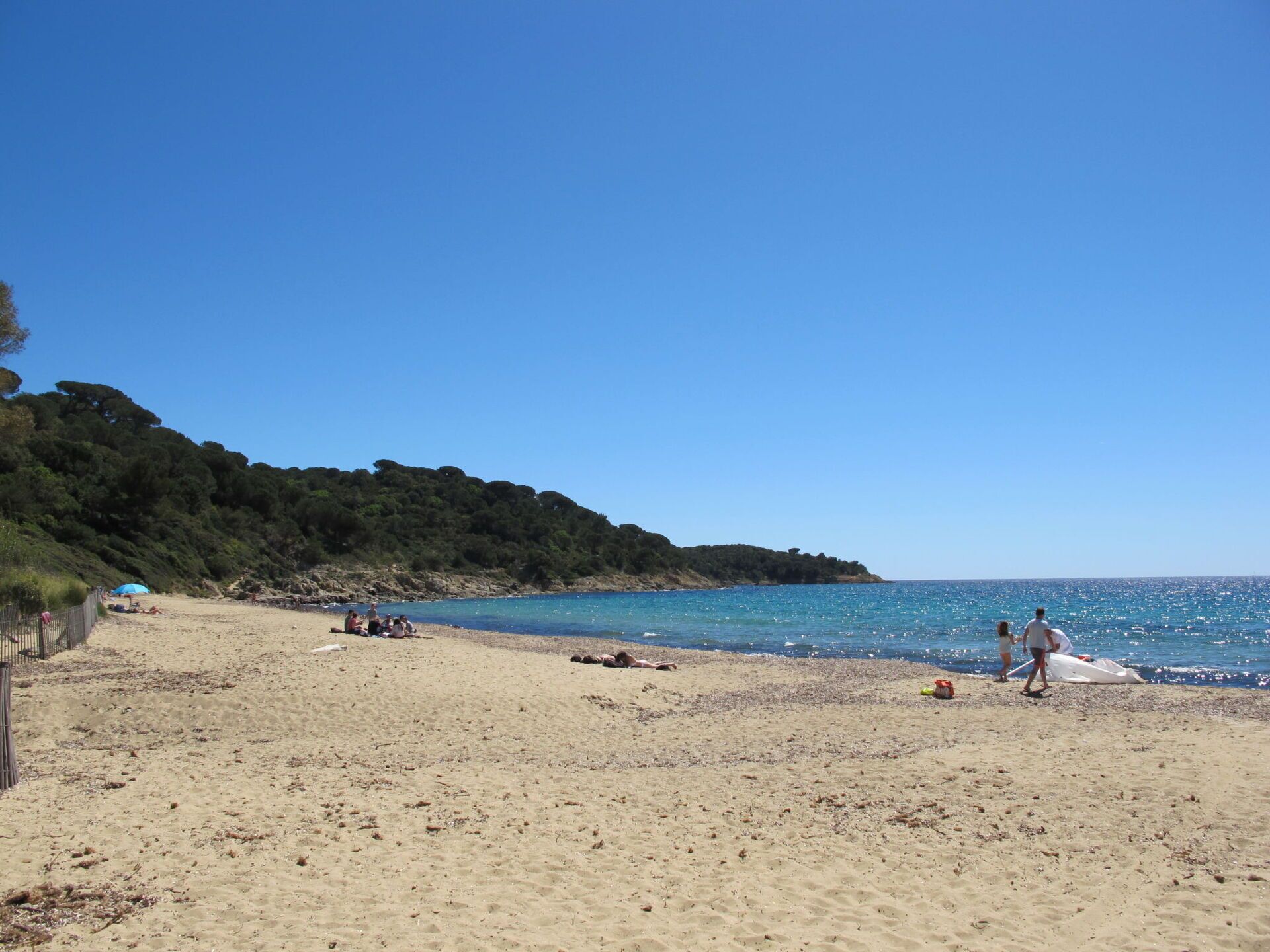 Une plage avec un ciel dégagé, un rivage sablonneux et quelques personnes qui se promènent.