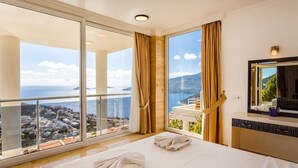 Hotelkamer met een ruim balkon, een bed met handdoeken, een spiegel en uitzicht op zee en de stad.