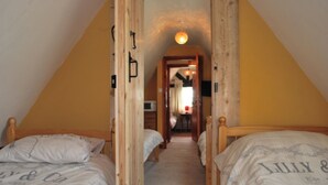 A narrow attic bedroom with two wooden beds, a sloped ceiling, and a small hallway leading to a dining area.