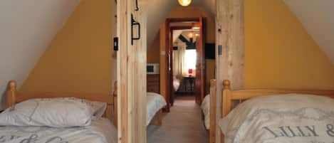 A narrow attic bedroom with two wooden beds, a sloped ceiling, and a small hallway leading to a dining area.
