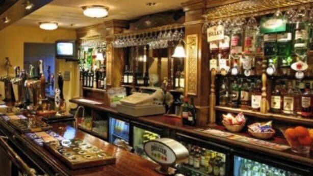 A bar area with a variety of liquor bottles, a cash register, and a refrigerated display case.
