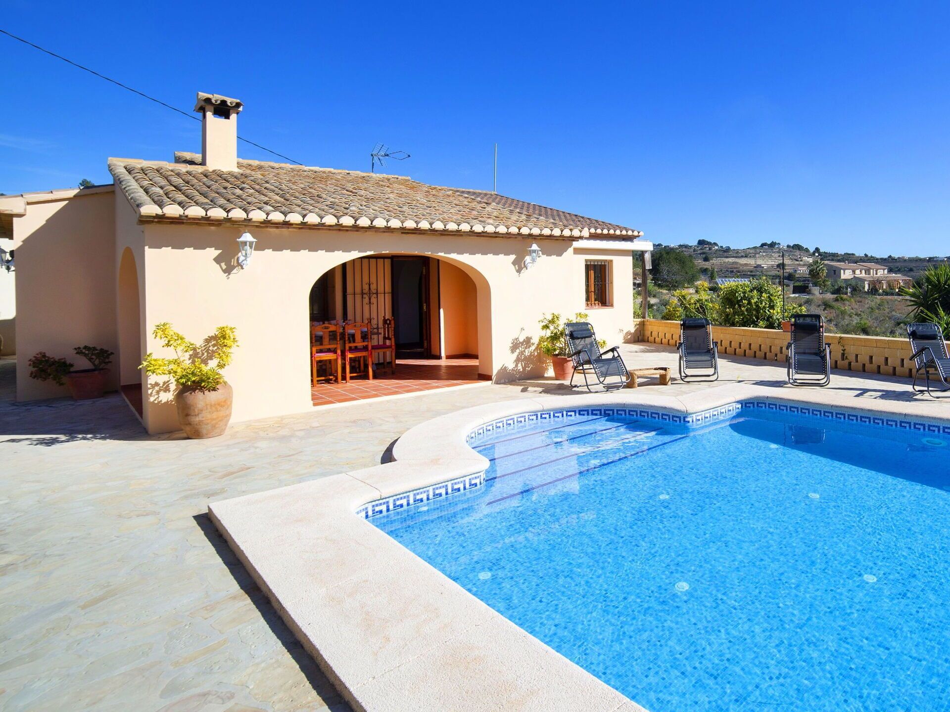 Ein Pool mit gefliestem Rand, eine Terrassenanlage mit Liegestühlen und ein Gebäude mit einem Bogenportal.
