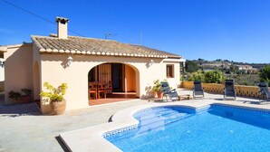 Una piscina con borde de azulejos, un área de patio con sillas de descanso y un edificio con un arco de entrada.