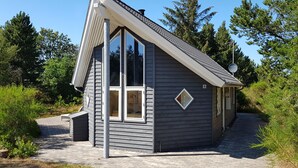 Una cabaña pequeña y moderna con techo inclinado, ventanas grandes y una antena parabólica.