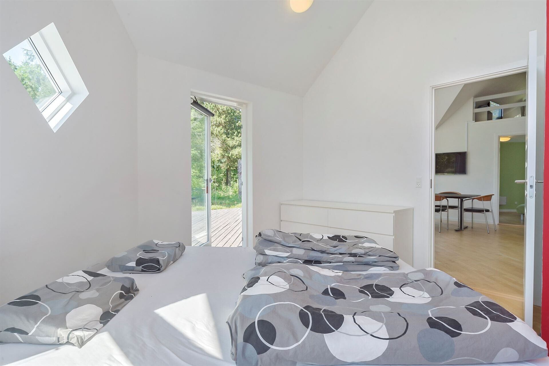 A bedroom with a bed, a window, and a door leading to another room.