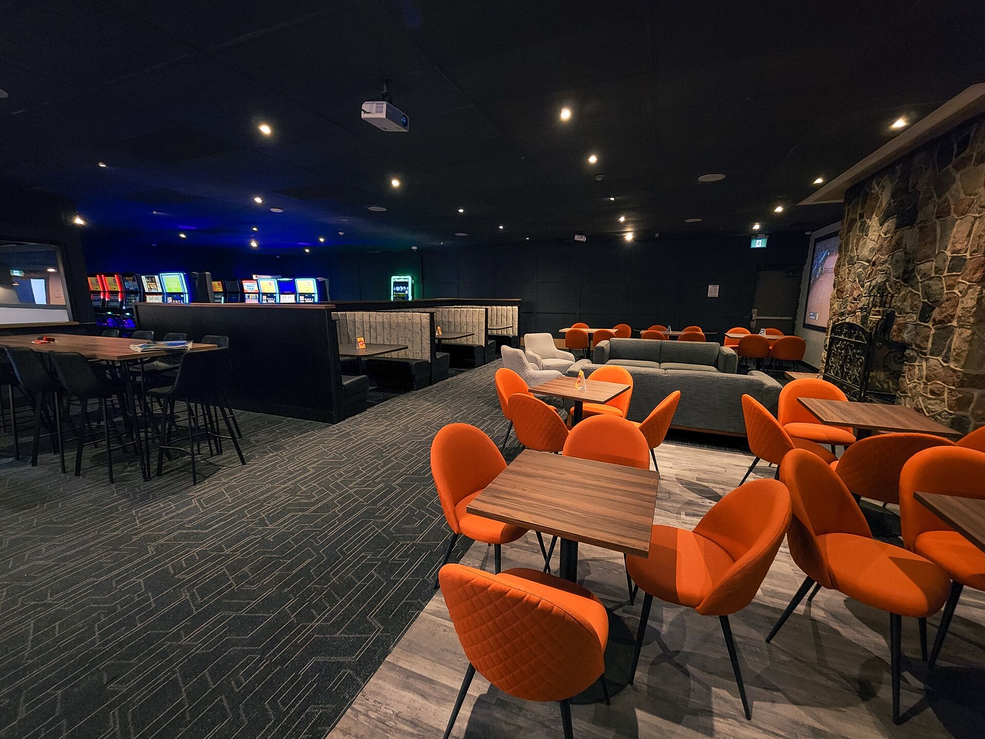 A modern lounge area with orange chairs, a stone accent wall, and a bar area with gaming machines.