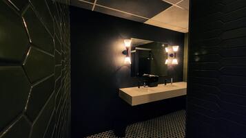 Un baño moderno con una pared oscura, un piso de diseño geométrico y un tocador blanco con un espejo y dos luces empotradas.