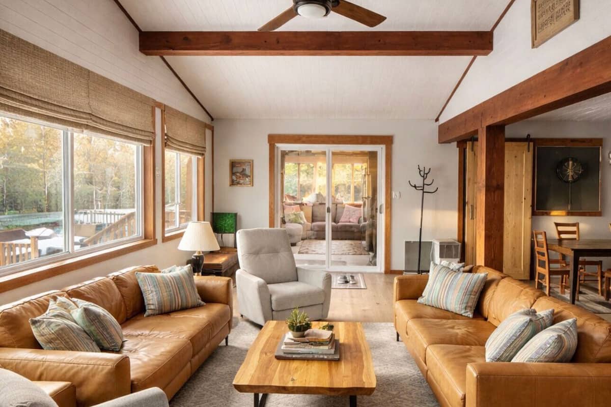 A spacious living room with leather sofas, a wooden coffee table, and a large window offering a view of the outdoors.