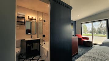 Un baño de hotel moderno con suelo de patrón geométrico, un lavabo con espejo y una silla roja junto a la ventana.