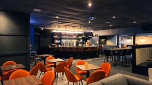 Zona de bar moderna con mostrador, asientos y una pantalla de proyección.