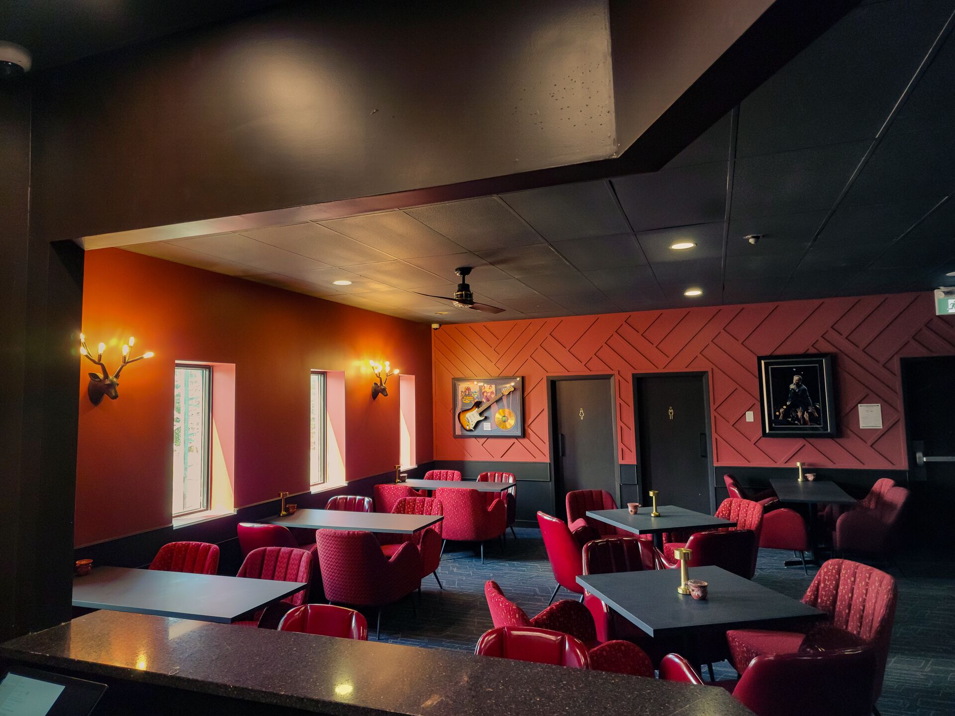 A restaurant with red chairs and tables, a wall-mounted deer head light, and a ceiling fan.