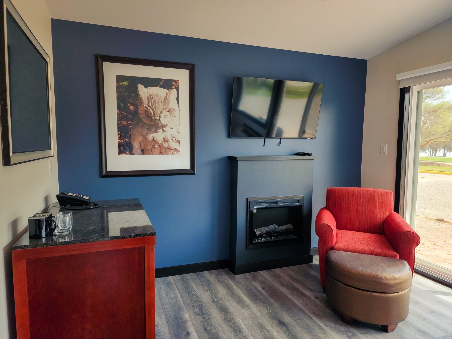 Un salon moderne avec un mur bleu, une cheminée, un fauteuil rouge et un téléviseur fixé au-dessus de la cheminée.
