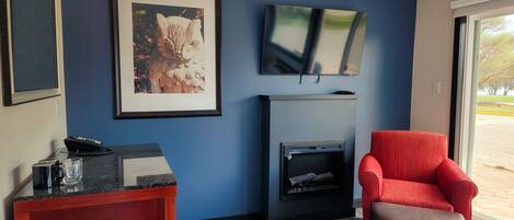 Un salon moderne avec un mur bleu, une cheminée, un fauteuil rouge et un téléviseur fixé au-dessus de la cheminée.