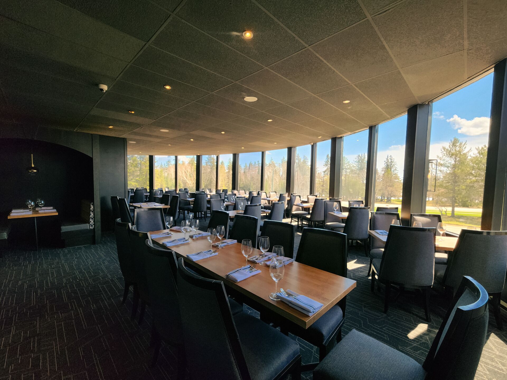 Une salle de conférence dotée d’une longue table, de chaises et de grandes fenêtres donnant sur un paysage arboré et le ciel.