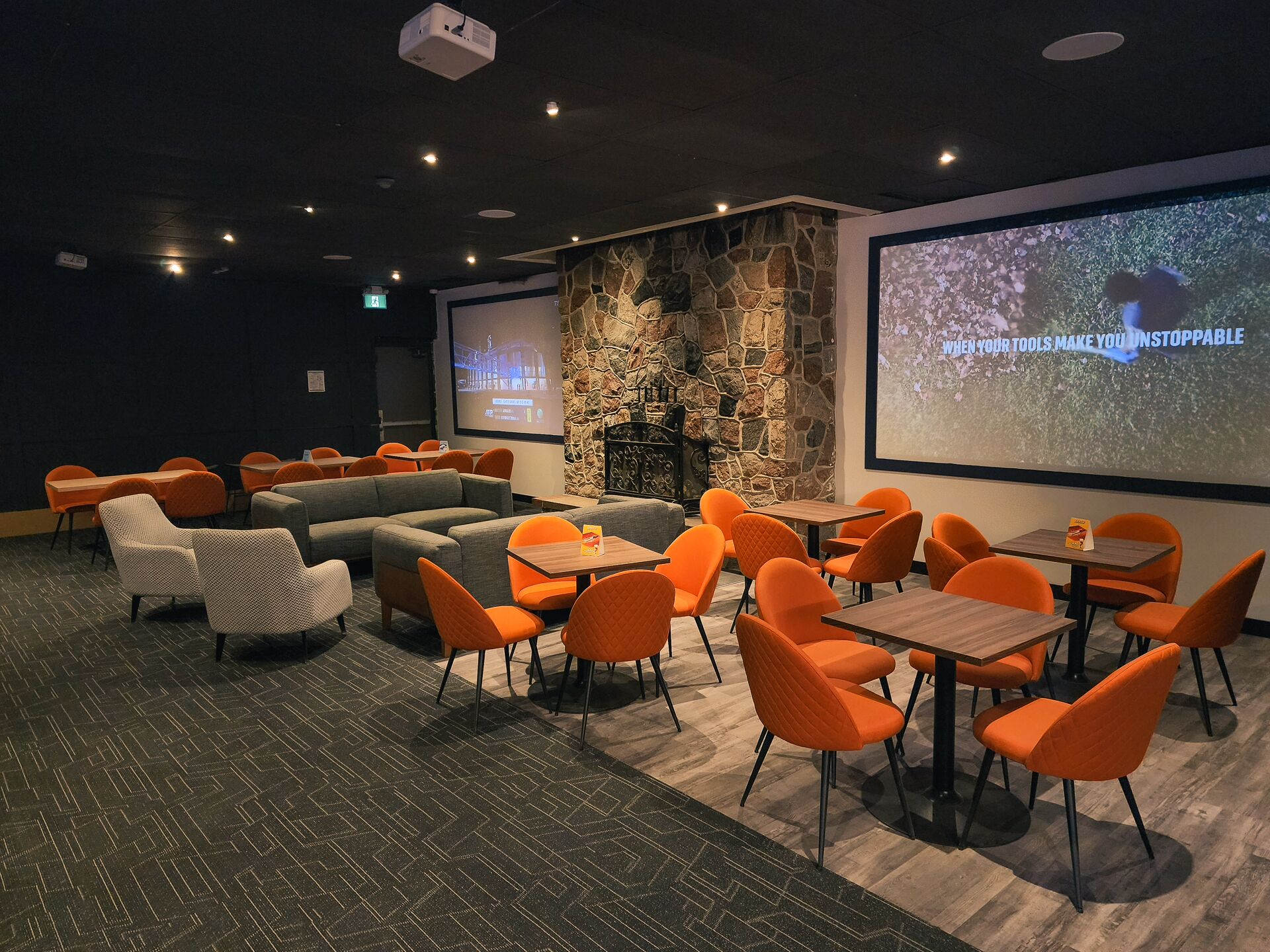 A conference room with a stone wall, a fireplace, orange chairs, and tables.