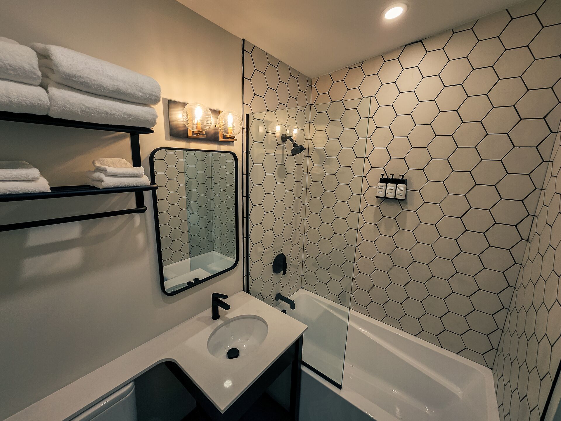 Une salle de bain moderne avec un revêtement mural en carreaux hexagonaux, un grand miroir, un lavabo et une baignoire.