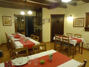 A dining area with multiple tables set for meals, wooden chairs, and a wooden ceiling.