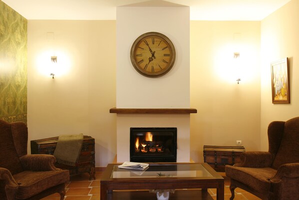 A living room with a fireplace, two armchairs, a coffee table, and a wall clock.