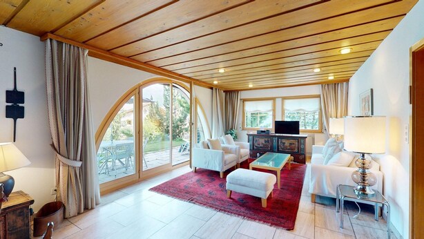 A spacious living room with a wooden ceiling, large windows, and a television. - Authentic semi-detached holiday home in a quiet location on the outskirts of Cel (Celerina/Schlarigna)