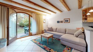 Ein Wohnzimmer mit einer Couch, einem Couchtisch, einem gemusterten Teppich und einer Glastür, die in einen Garten führt.