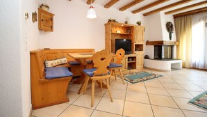 Ein gemütliches Wohnzimmer mit einer Holzbank, Sesseln, einem Fernseher und einem Kamin.