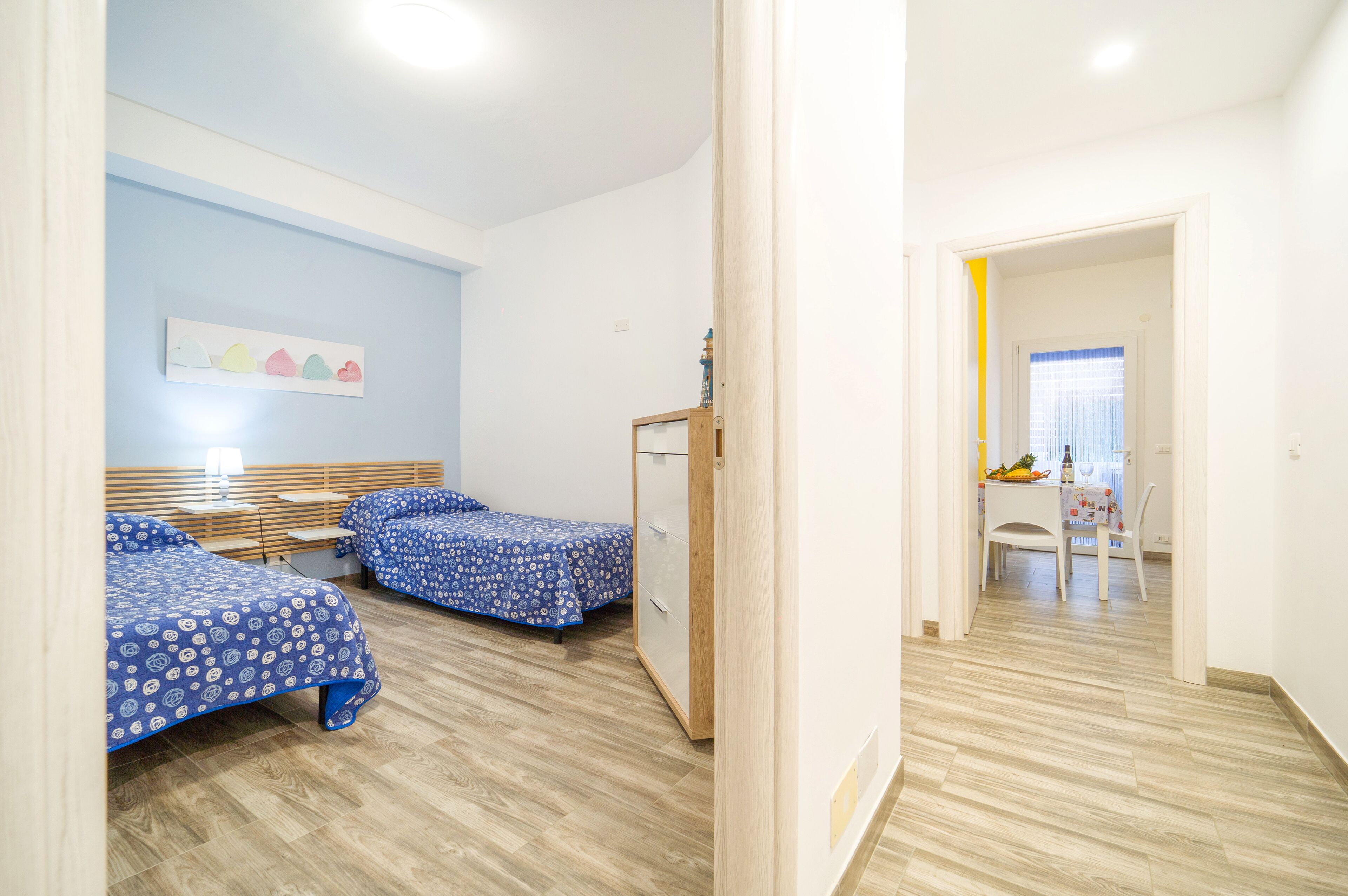 A room with two beds, a wooden wardrobe, and a small table with a chair.