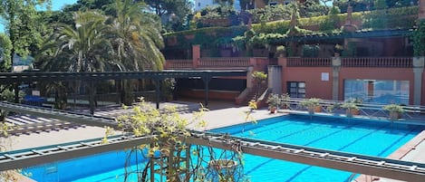 Una piscina con solárium de baldosas, rodeada de plantas en macetas y árboles.
