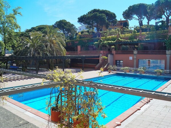 A swimming pool with a tiled deck, surrounded by potted plants and trees.