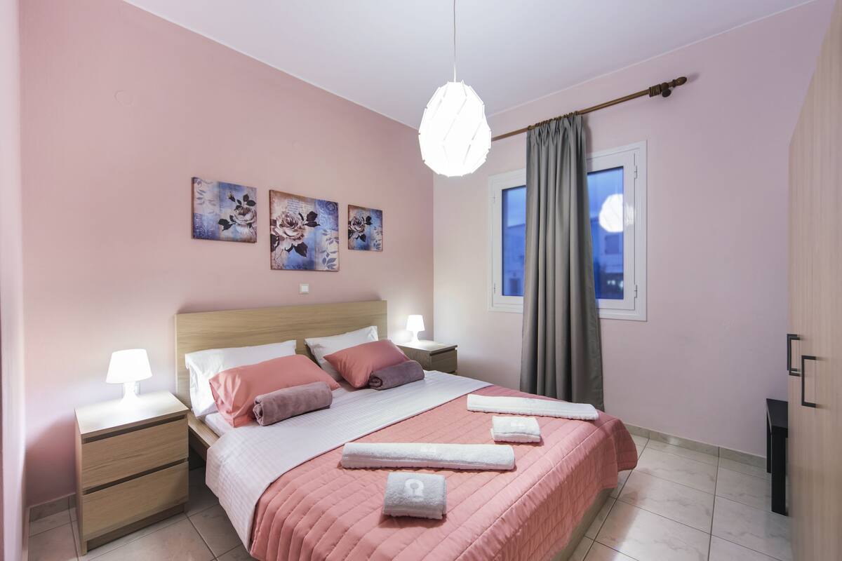 Ein Schlafzimmer mit Bett, Nachttischen, einer Lampe und einem Fenster mit Vorhängen.