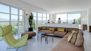 Un salon spacieux avec une grande fenêtre, un cactus, un canapé et un fauteuil.
