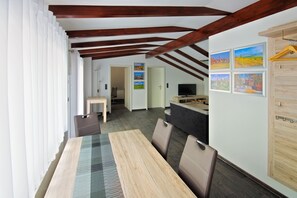 Ein Essbereich mit einem Holztisch und Stühlen, einem Sofa und einem Fernseher. An den Wänden befinden sich gerahmte Bilder und ein Holzschrank.