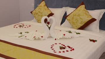 Una cama con colcha blanca y amarilla, dos almohadas con forma de cisne y arreglos de pétalos de rosa en forma de corazón.