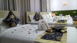 Habitación de hotel con dos camas, cada una con cabecero, ropa de cama blanca y almohadas decorativas. Hay luces fijadas en la pared y una mesita de noche con lámpara.