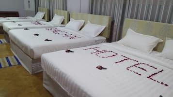 Een hotelkamer met vier bedden, elk voorzien van witte lakens en rozenblaadjes.