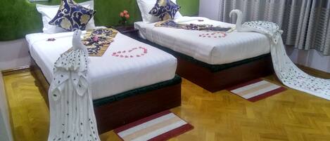 Dos camas individuales con cabeceros verdes, ropa de cama blanca y almohadas decorativas.