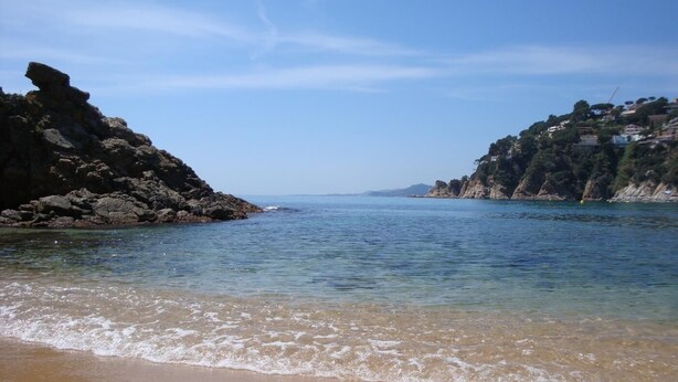 Una spiaggia con acque cristalline, scogliere rocciose e edifici sulle colline.