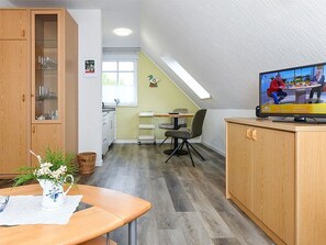 Eine moderne Küche mit Holzschränken, ein Essbereich mit Tisch und Stühlen sowie ein Fernseher an der Wand.