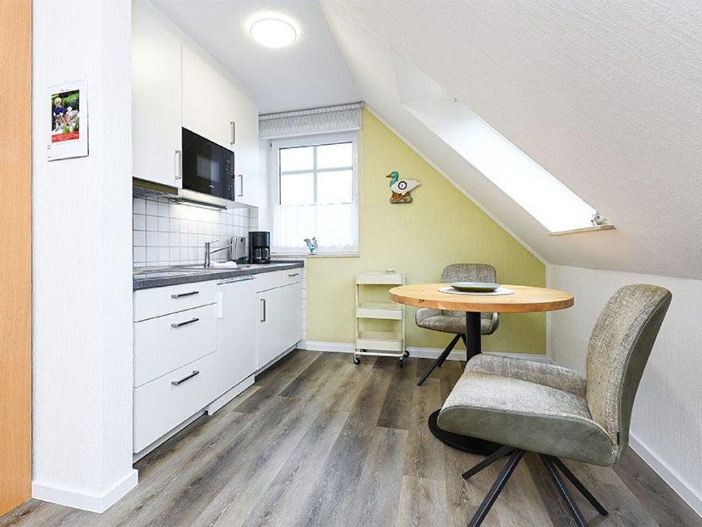 Une cuisine compacte avec des meubles blancs, un four à micro-ondes et une petite table à manger avec deux chaises.