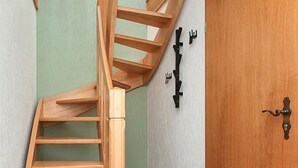 Een houten trap die leidt naar een kamer met een houten deur en een lichtschakelaar aan de muur.