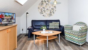 Een moderne woonkamer met een houten salontafel, een donker leren bank, een fauteuil met een patroon en een plafondlamp.