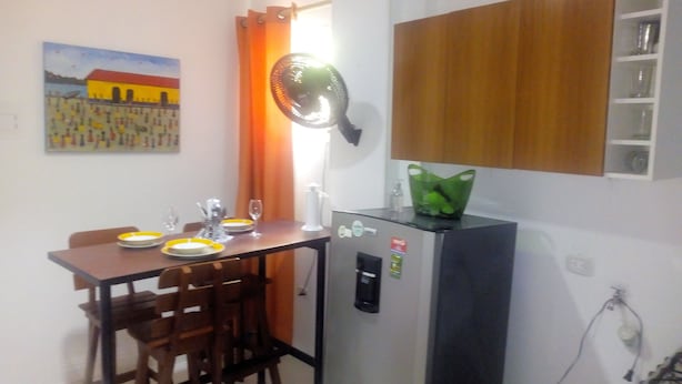 Eine kleine Küche mit einem Kühlschrank, einem Esstisch mit Stühlen und einem Bild an der Wand.