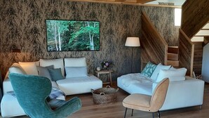 Un salon moderne doté d’un grand téléviseur, de deux canapés, d’un fauteuil original et d’un escalier en bois.