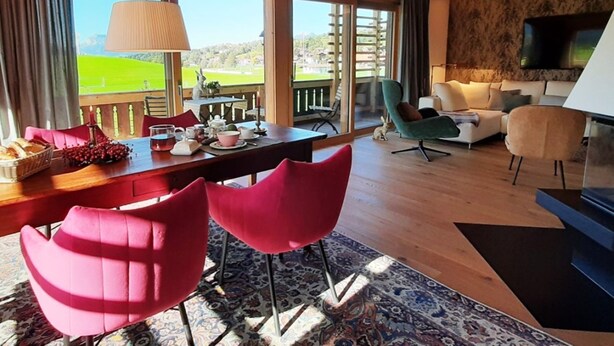 Un salon moderne avec un plafond en bois, un coin repas avec des chaises rouges, un canapé et un téléviseur.