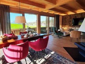 En moderne stue med træloft, spiseplads med røde stole, sofa og fjernsyn.