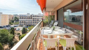 Un balcon avec une table dressée pour deux personnes, donnant sur un parking et des immeubles.