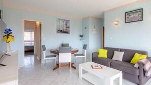 Un salon moderne avec un canapé gris, une table basse blanche et un coin repas comprenant une table ronde et des chaises.