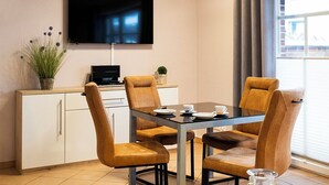Ein moderner Essbereich mit Tisch und vier Stühlen, einem an der Wand befestigten Fernseher und einem Fenster, das natürliches Licht hereinlässt.