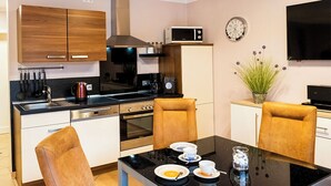 Eine moderne Küche mit schwarzem Arbeitsplatz, Edelstahlgeräten und Holzschränken. Ein Esstisch mit Stühlen und eine Uhr sind an der Wand zu sehen.