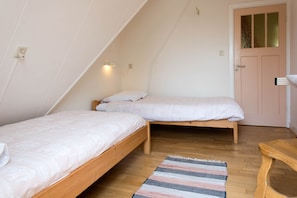 Quarto com duas camas de madeira, um tapete listrado e uma porta com painel de vidro.